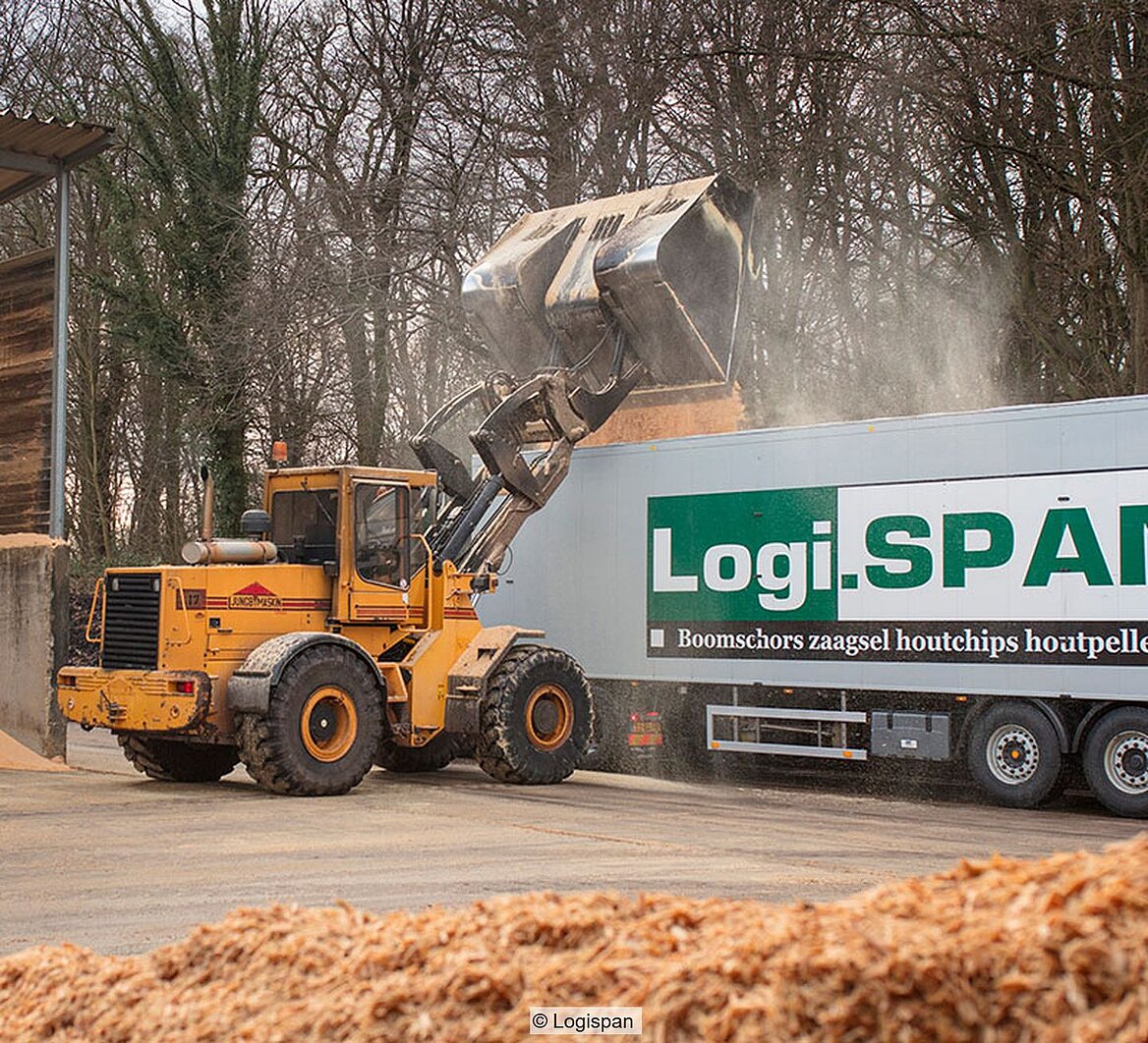 Radlader kippt Holzspäne in Lkw-Anhänger mit Aufdruck "Logispan)"