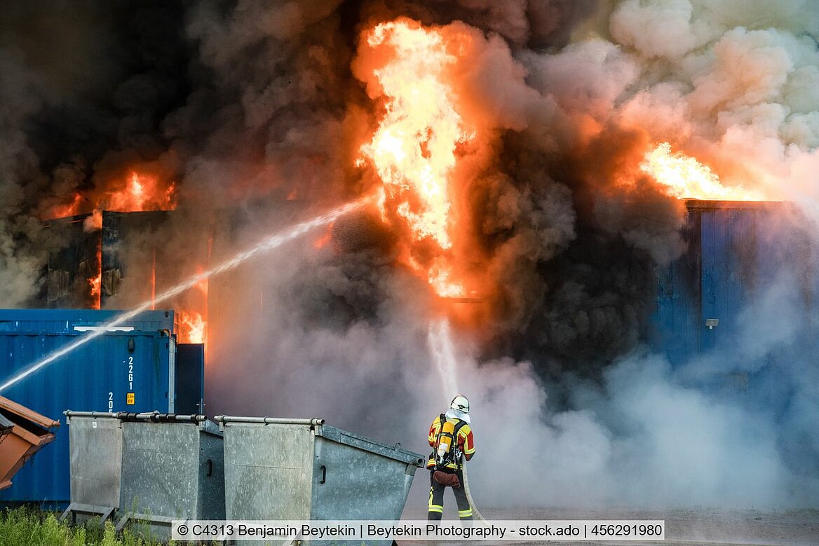 Symbolbild: Feuerwehrmann vor brennendem Industriegebäude