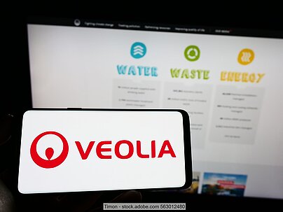Computerbildschirm mit den Logos der drei Veolia-Geschäftsbereiche Wasser, Abfall und Energie, im Vordergrund Handy-Bildschirm mit dem Konzernlogo. 