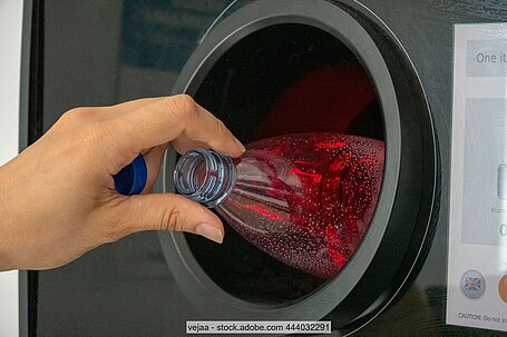 Hand steckt Plastikflasche in Öffnung von Pfandautomat