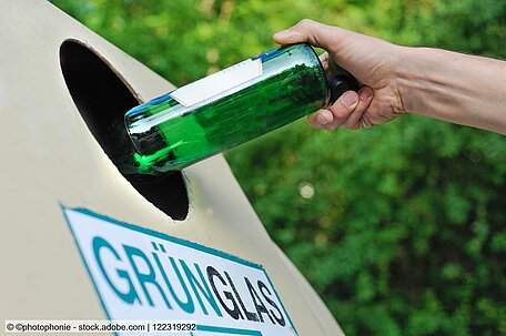 Eine Hand wirft eine grüne Flasch in einen Altglascontainer.