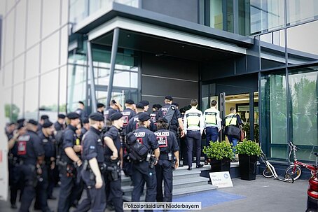 Große Gruppe Polizisten in Uniform und teilweise auch nur gelben Warnwesten mit Aufschrift "Polizei" vor Bürogebäude