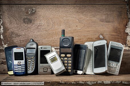 Mehrere alte Mobiltelefonie liegen in einem Holzregal  