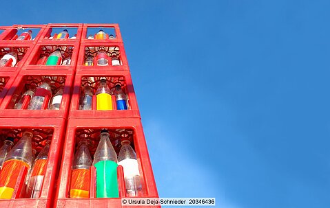 Stapel von roten Getränkekästen mit leeren Mehrweg-Kunststoffflaschen vor blauem Himmel