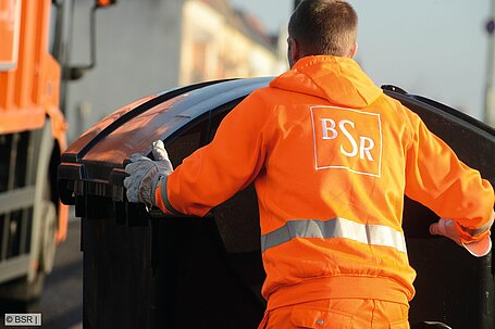 BSR-Müllwerker schiebt Abfallcontainer