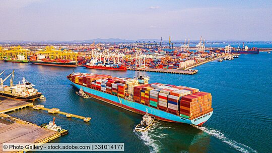 Containerschiff im Hafen, im Hintergrund Hafenanlage und weitere Schiffe