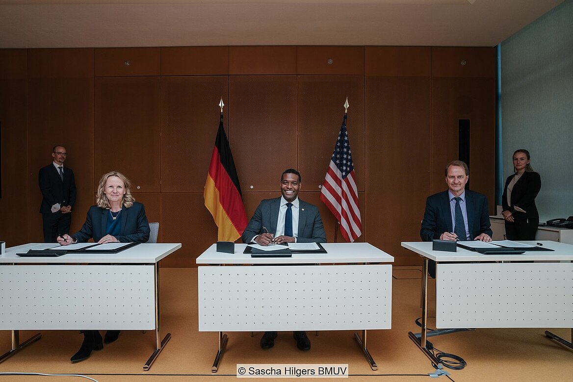 Umweltministerin Lemke, EPA-Leiter Regan und UBA-Präsident Messner sitzen an Tischen vor Flaggen von Deutschland und den USA und unterzeichnen Erklärung