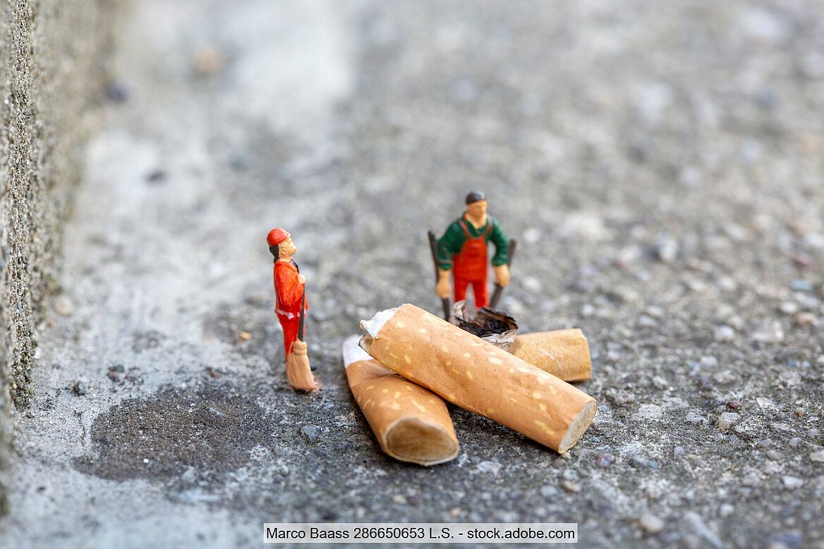 Müllmänner als Spielzeugfiguren neben Zigarettenstummel auf Straße