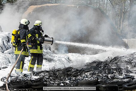 Zwei Feuerwehrmänner löschen ein Feuer mit einem Schlauch.