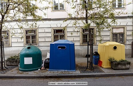 Grüner, blauer und gelber Abfallcontainer auf Straße vor Haus in Zagreb, dazwischen Bäume und Müllsäcke