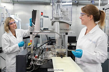 Zwei Forscherinnen in weißen Kitteln stehen in einem Labor.