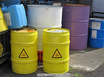 Mehrere Stahlfässer in unterschiedlichen Größen und Farben. Zwei von ihnen tragen das gelbe "Totenkopf"-Warnzeichen für giftige Stoffe.  