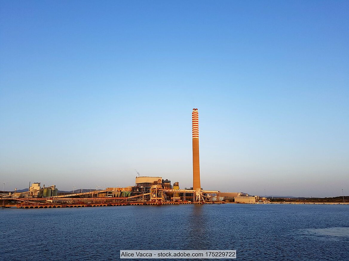 Blick von Meer auf Industrieanlage Portovesme, dahinter blauer Himmel