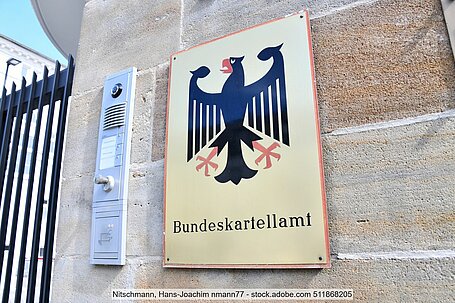 Schild mit Bundesadler und Aufschrift "Bundeskartellamt" an Mauer neben Klingelanlage und Metallstreben von Eingangstor