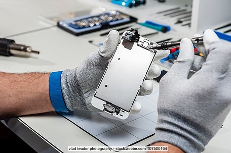 Zwei behandschuhte Hände mit Werkzeug bei Reparatur von Mobiltelefon