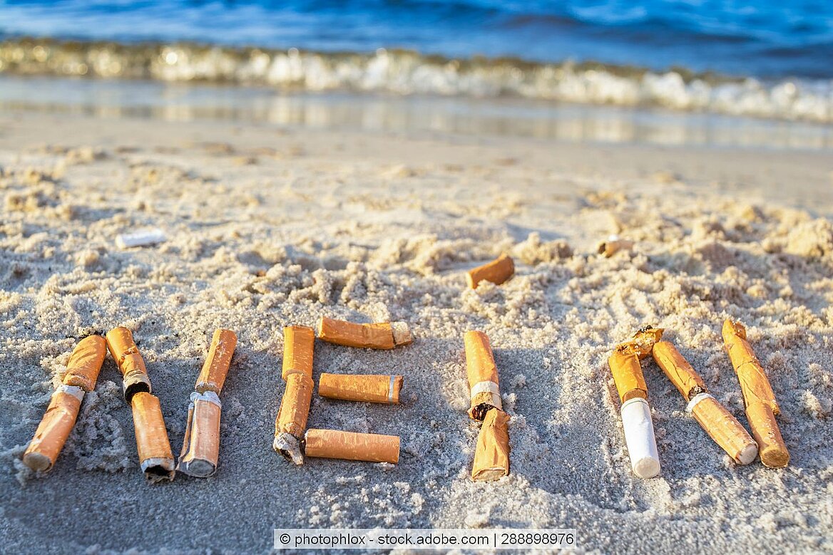 Zigaretten liegen zu einem "Nein" geformt am Strand.