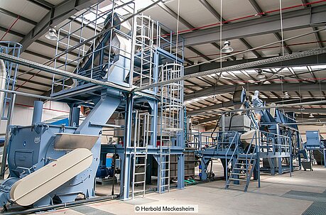 Blau gestrichene Industrieanlage mit Förderbändern, Rohren Trichtern, Kesseln, Treppen in Fabrikhalle