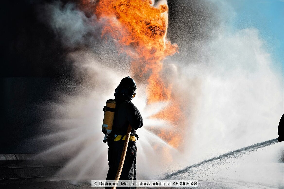Feuerwehrmann hält den Schlauch auf ein Feuer und löscht es.