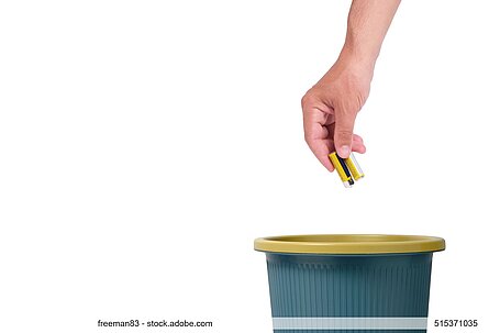 Hand mit kleinen Batterien über Mülltonne vor weißem Hintergrund