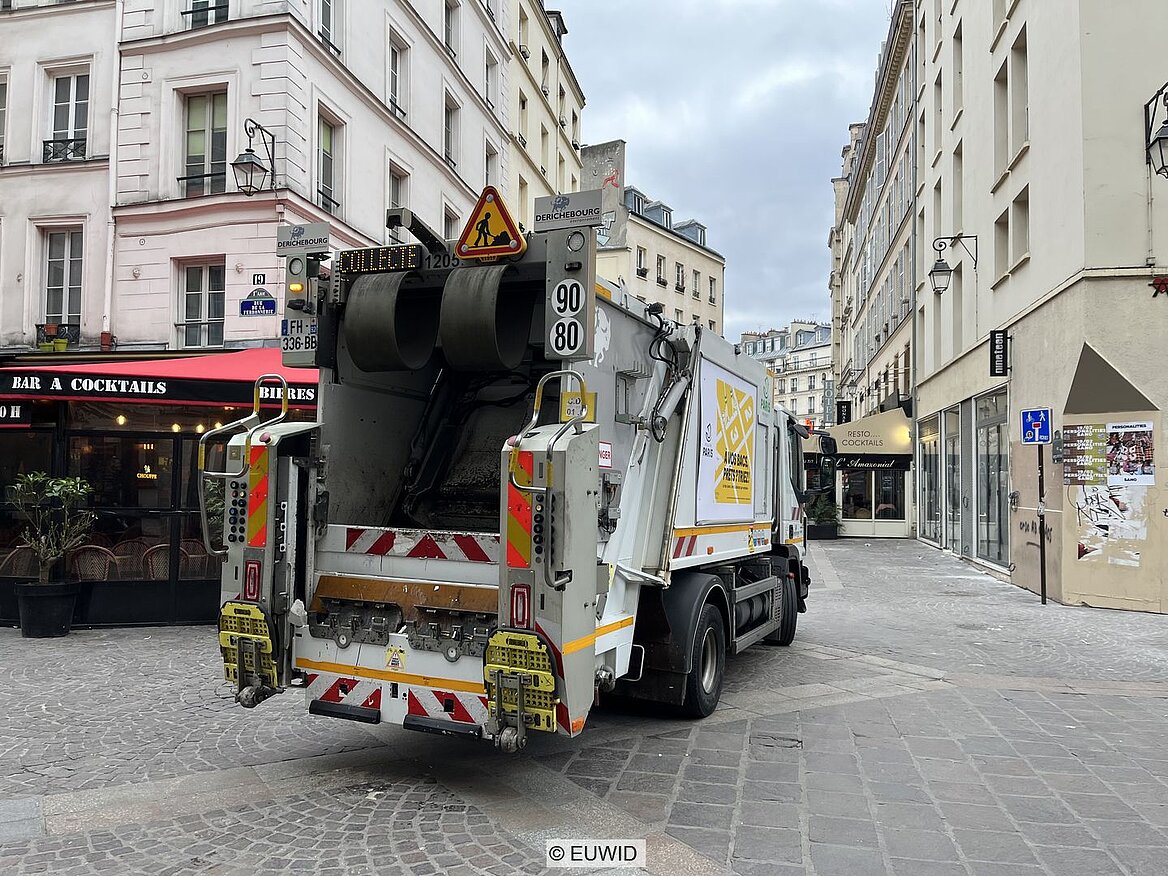 Müllfahrzeug auf Straße zwischen zwei Restaurants in Pariser Stadtzentrum