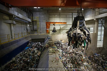 Metallgreifarm voll mit Müll über Abfallberg in Industriehalle