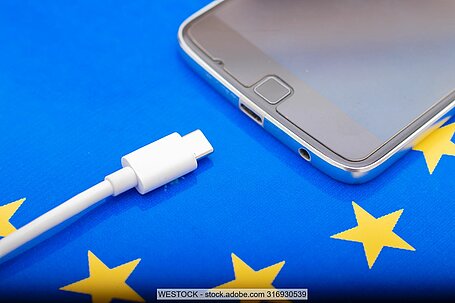 Weißes Ladekabel mit USB-Anschluss vor Handy und auf EU-Flagge