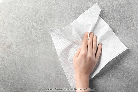 Hand, die eine graue Oberfläche mit einem Papierhandtuch abwischt.