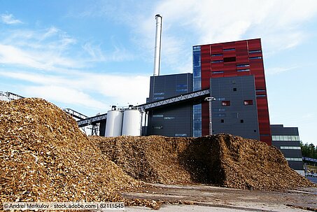 Symbolbild: Biomasseheizkraftwerk vor Hackschnitzelhaufen