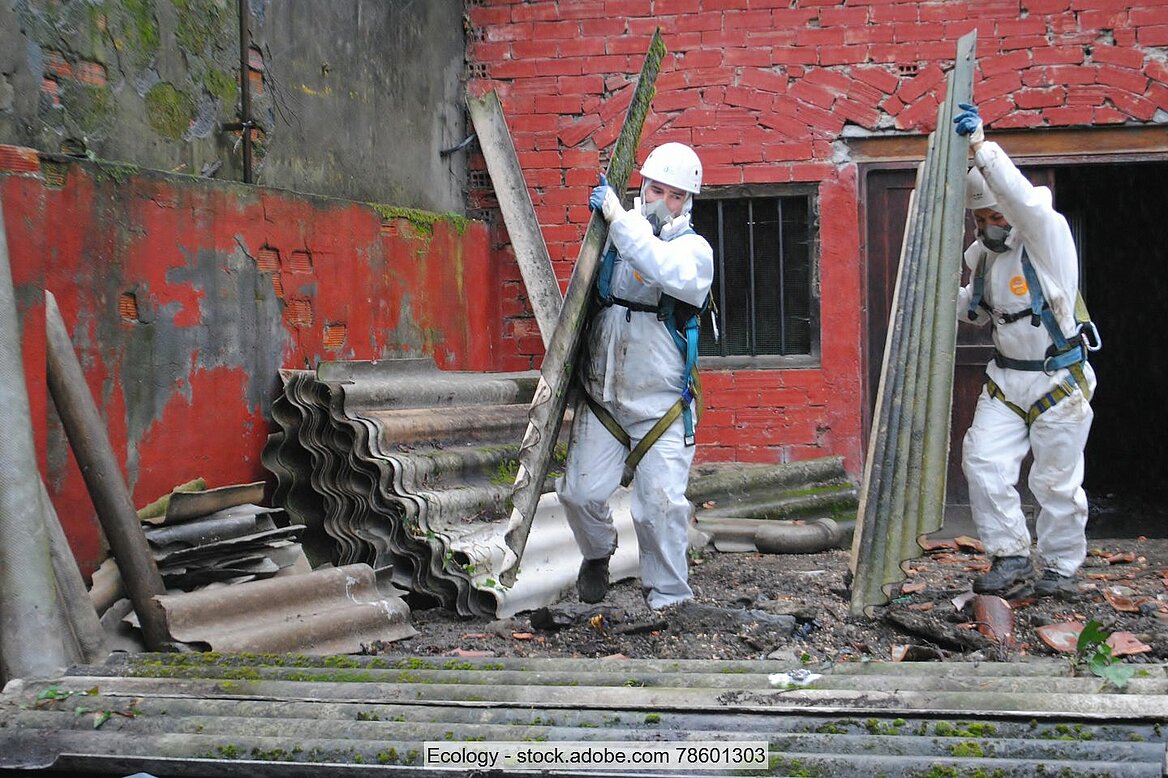 Männer in Schutzanzügen mit Atemmasken tragen asbesthaltige Abbruchstücke auf Baustellen