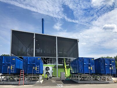 Vier blaue Container stehen vor dem Neubau der EAD-Karbonisierungsanlage