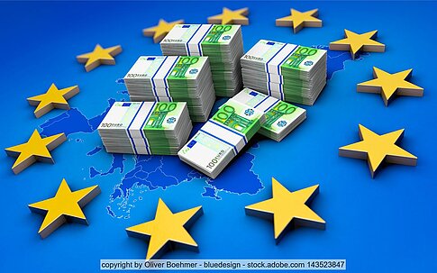 Bündel von Euro-Scheinen umringt von gelben Sternen der EU-Flagge auf blauem Untergrund