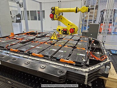 Gelber Roboterarm über Batteriesystem in einer Halle