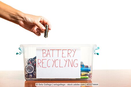 Eine Batterie wird von einer Hand in ein Behältnis mit vielen weiteren Batterien gelegt.