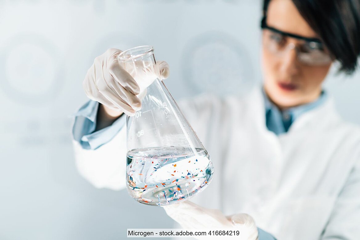 Wissenschaftlerin schaut sich Reagenzglas an. Darin ist eine Wasserprobe mit Mikroplastik.