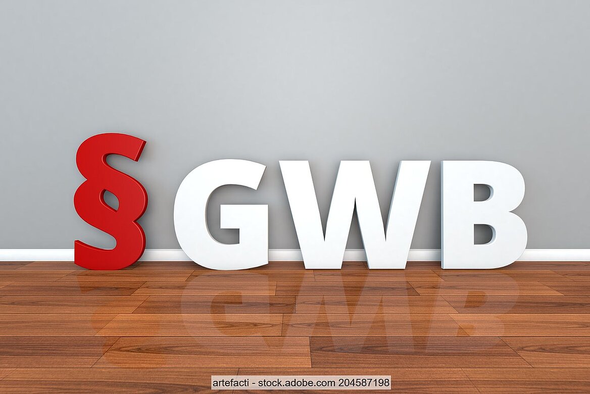Rotes Paragraphen-Symbol neben weißen Buchstaben "GWB" vor grauem Hintergrund und über Holzuntergrund