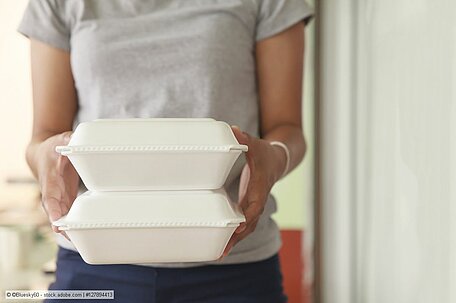 Eine Frau trägt zwei Essensverpackungen aus Polystyrol 