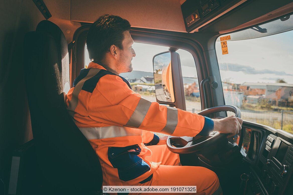 Fahrer in orangener Arbeitskleidung sitzend hinter Lenkrad von Müllauto