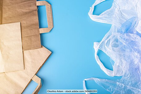 Einkaufstüten aus braunem Papier und Einwegbeutel aus durchsichtigem Kunststoff auf hellblauem Hintergrund