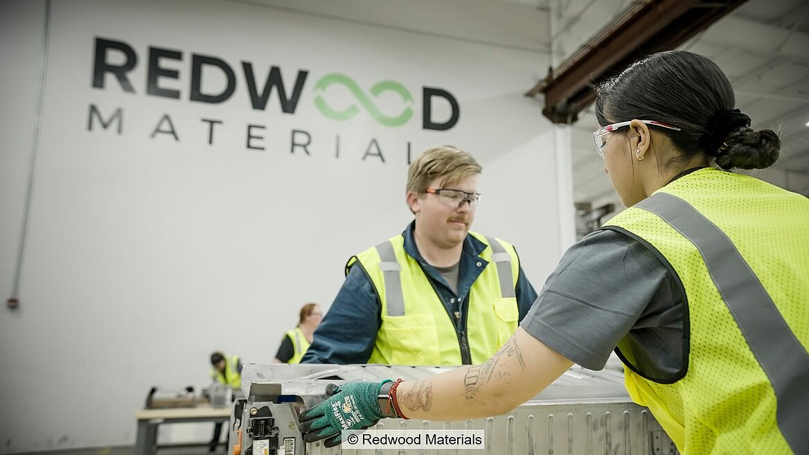 Zwei Mitarbeiter von Redwood Materials bauen einen E-Autoakku auseinander.