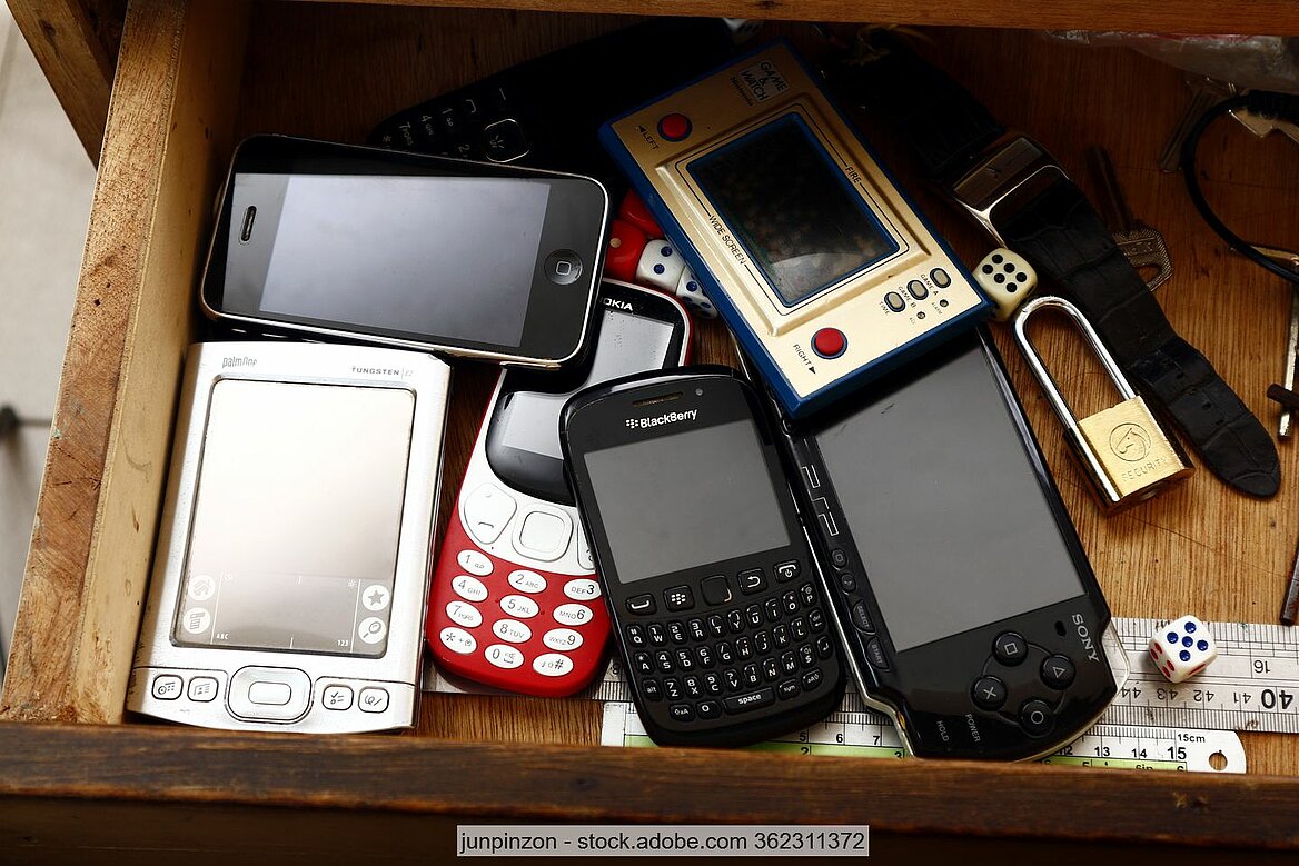 Verschiedene Mobiltelefone, Smartphones und andere Kleingeräte in brauner Holzschublade