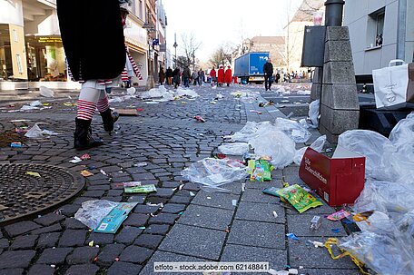Pflaster in Fußgängerzone mit Müll nach Faschingsumzug, im Hintergrund teilweise verkleidete Menschen