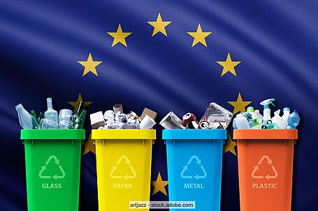 Vier farbige Mülltonnen mit unterschiedlichen Verpackungsabfällen mit einer Europaflagge im Hintergrund