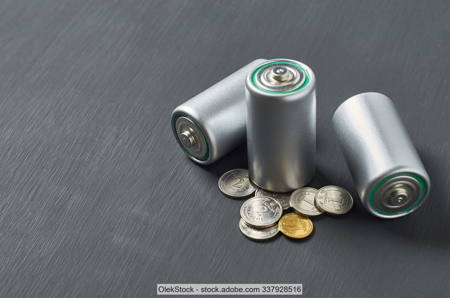 Drei kleine zylindrische silberne Batterien und verschiedene Münzen.