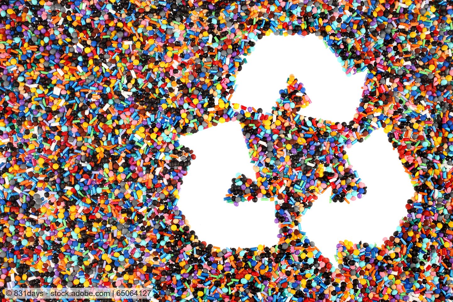 Recyclingsymbol mit drei Pfeilen vor Hintergrund aus bunten Kunststoffpellets.