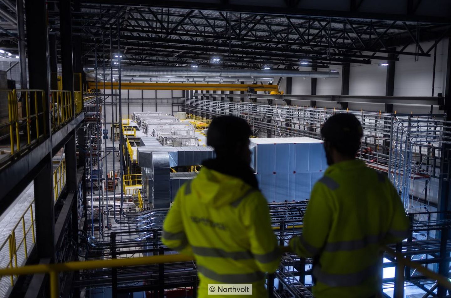 Blick in Produktionshalle, im Vordergrund zwei Personen in gelben Jacken mit Aufschrift "Northvolt"