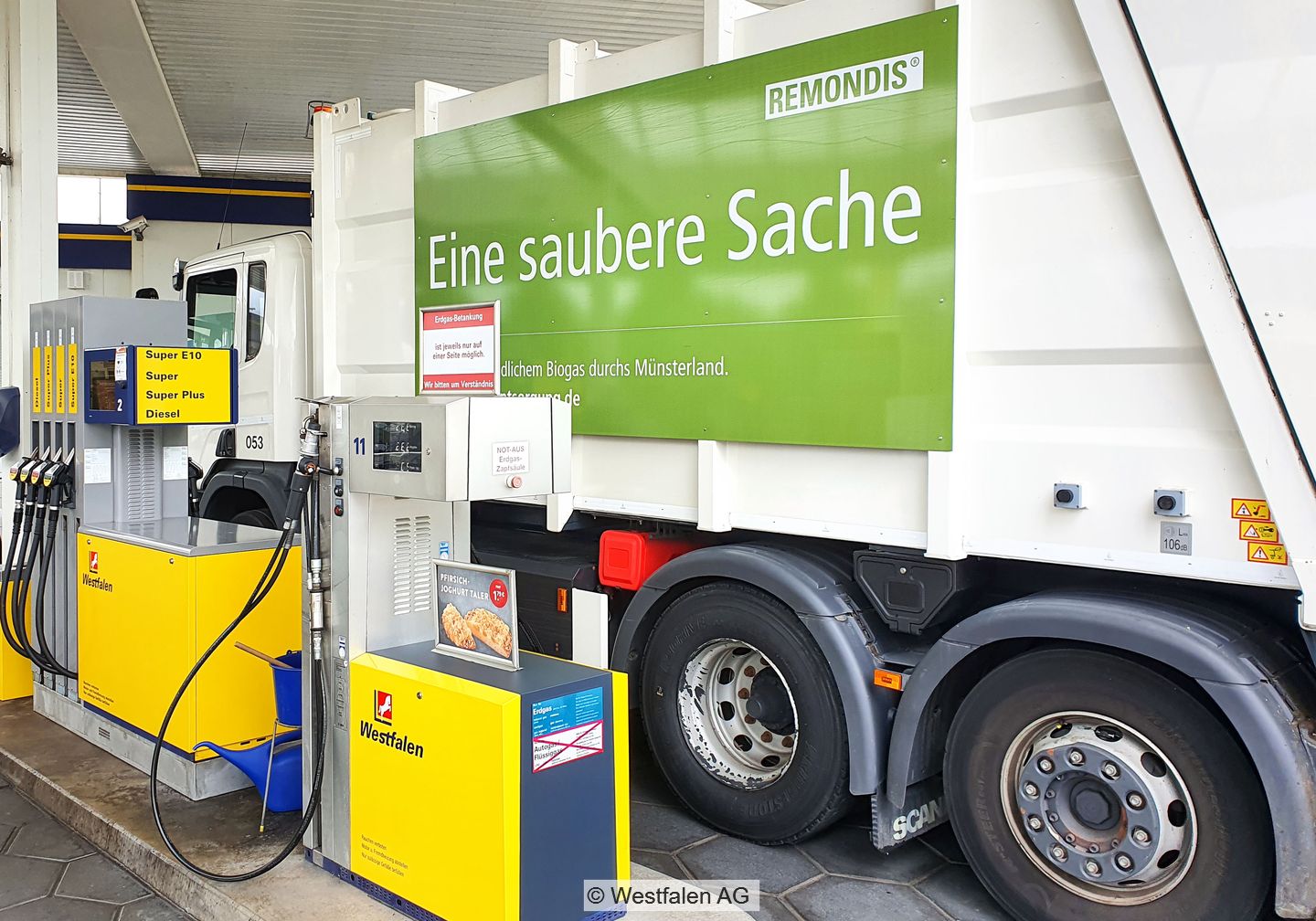 Weißes Müllsammelfahrzeug von Remondis mit großem grünen Aufdruck an Tankstelle mit Zapfsäulen der Westfalen AG