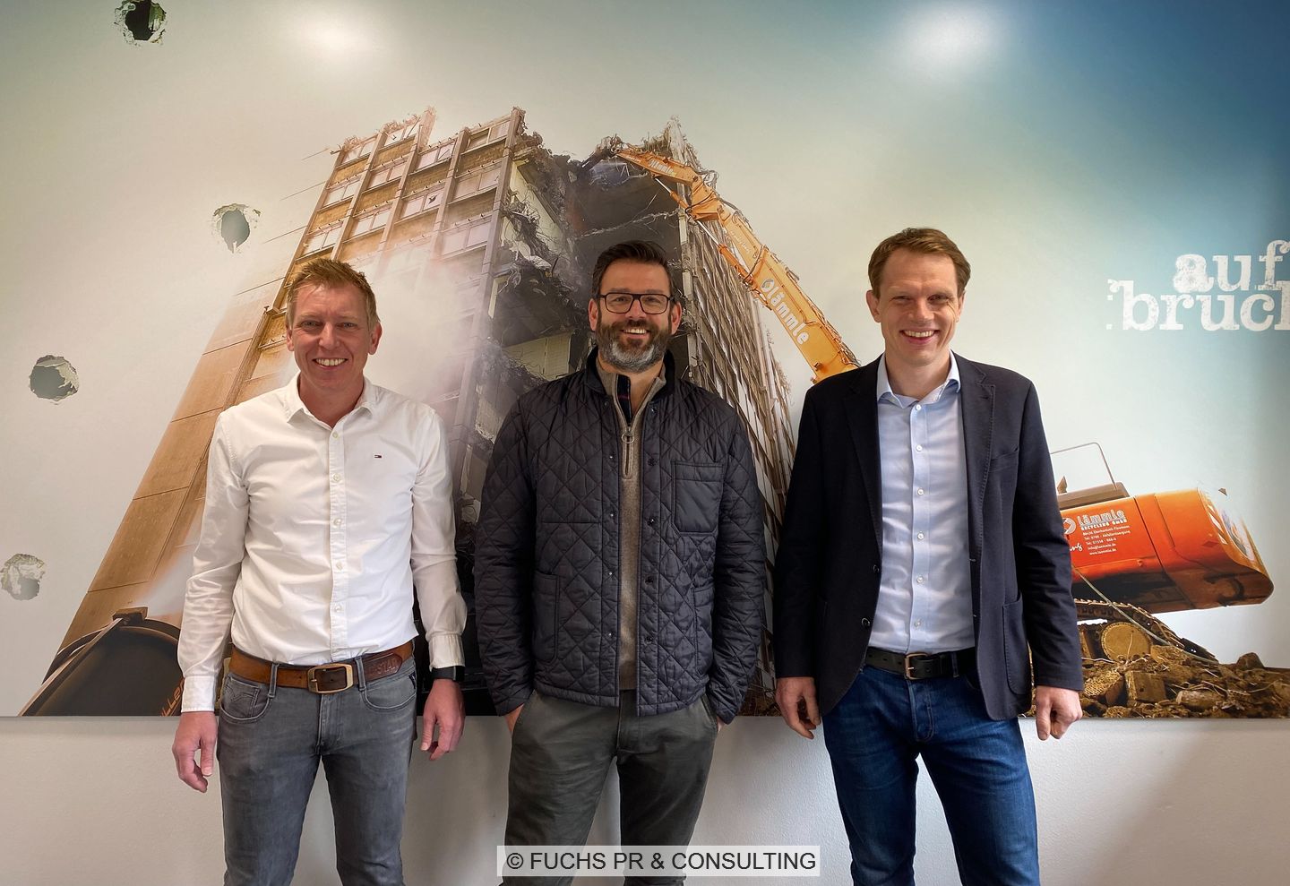 Zu sehen sind: Tobias Kuhn (KS Engineering GmbH), Stefan Lämmle (Lämmle Recycling GmbH) und Cassian Gruber (Geiger Unternehmensgruppe) vor einem Plakat eines abgebrochenen Gebäudes.