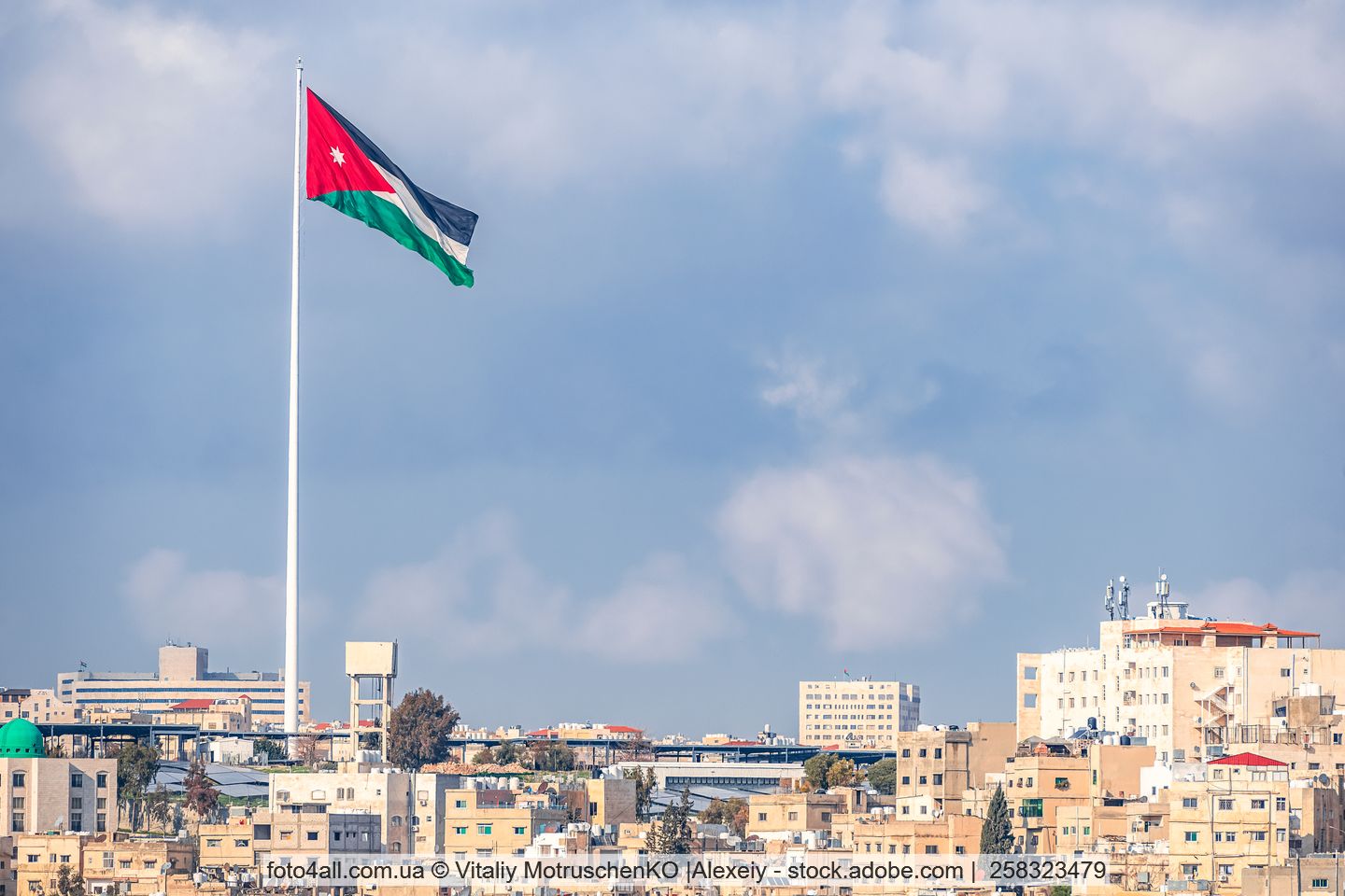 Die Flagge von Jordanien weht vor einer nahöstlich aussehnden Stadt.