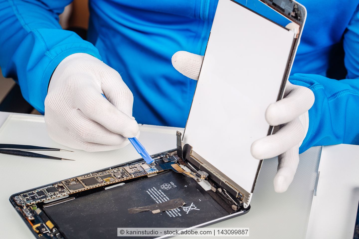Ein Tablet wird repariert von einer Person mit einem blauen Oberteil und weißen Handschuhen.